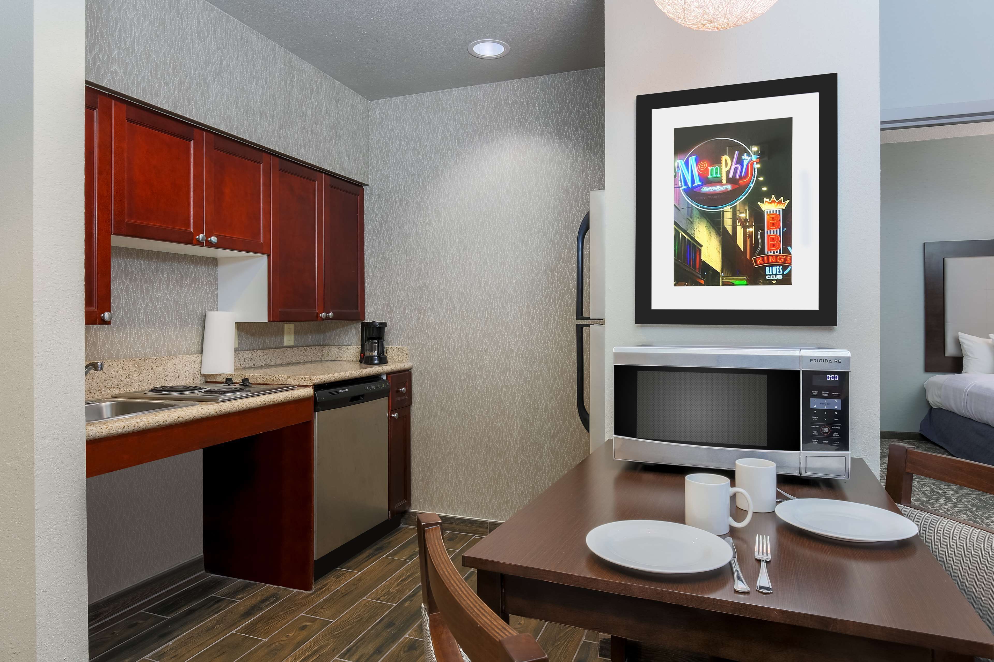 A compact kitchen with wooden cabinets, a microwave, and a dining table set for two.