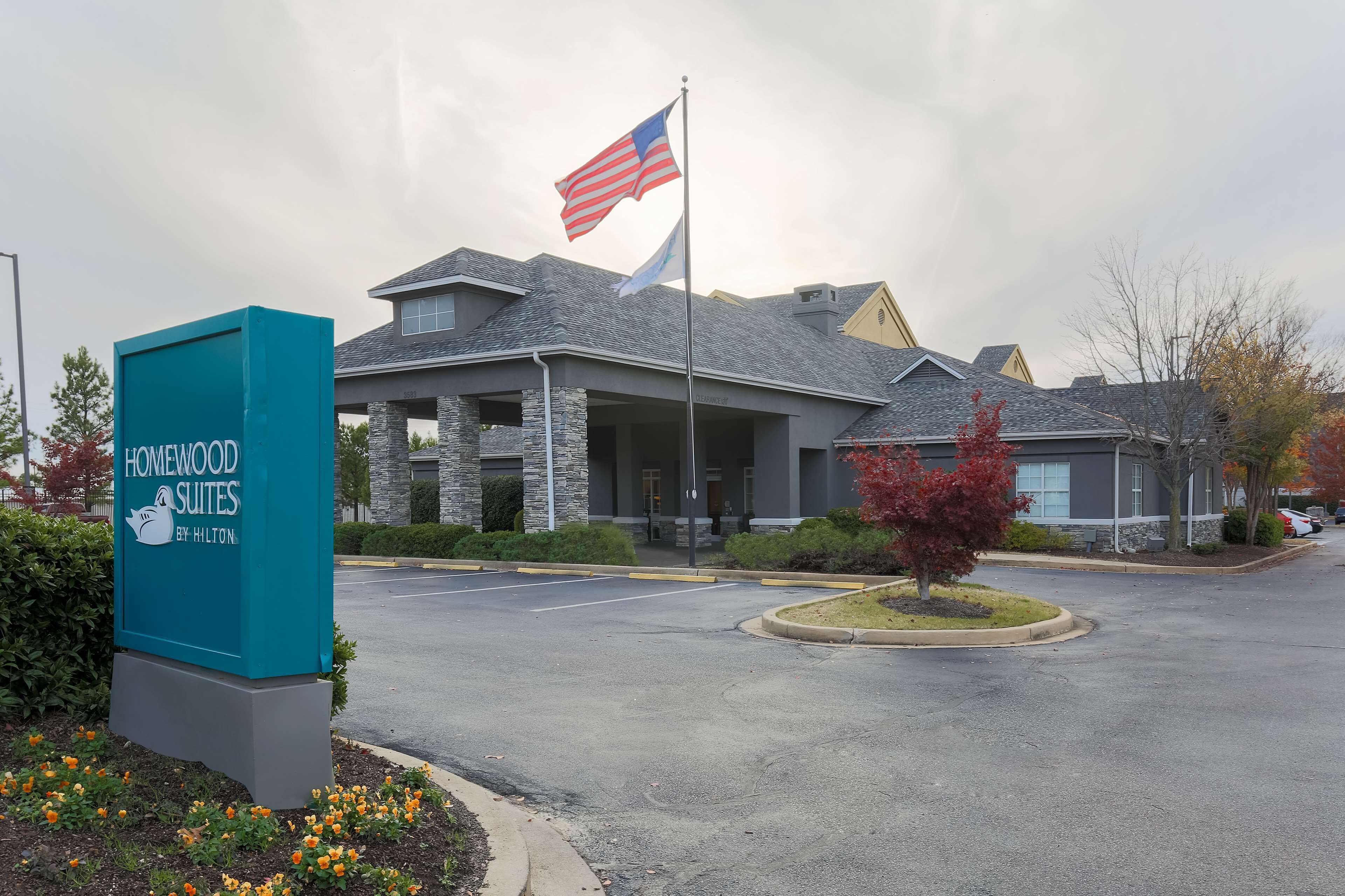 Een hotelingang met een bord voor Homewood Suites by Hilton, een vlag en een parkeerplaats.