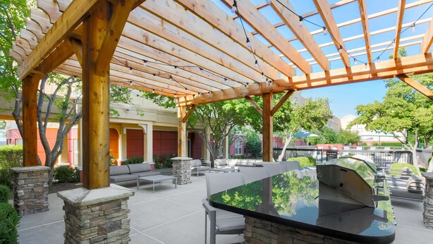 An outdoor patio area with a wooden pergola, stone pillars, a barbecue grill, and outdoor seating. - Homewood Suites Southwind - Hacks Cross (Memphis)