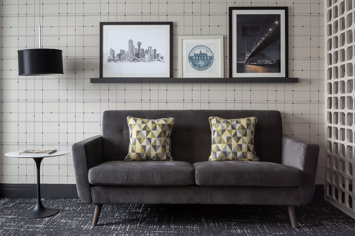 A grey sofa with patterned cushions, a framed cityscape picture, a framed circular logo, and a black pendant light.