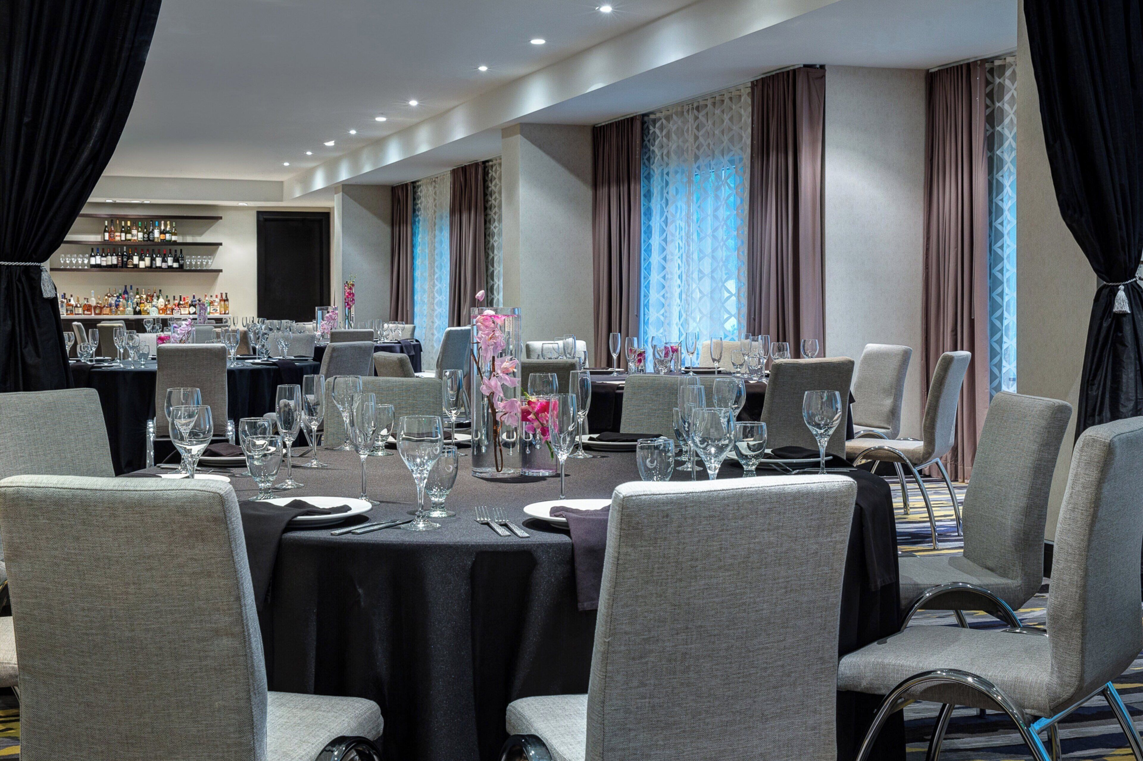 A dining area with tables set for a meal, chairs, and a bar with bottles in the background.