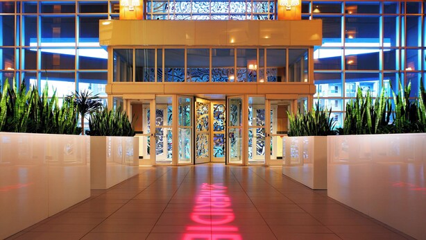 A hotel entrance with a glass facade, a central doorway, and a neon sign on the floor. - Le Meridien Dallas by the Galleria (Dallas)