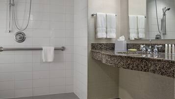 Un baño con ducha, toallero, lavamanos con encimera de granito y espejo.