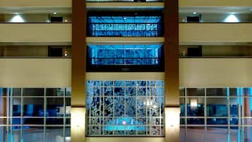 Eine mehrstöckige Hotelhalle mit einem zentralen Atrium, Glasgeländern und einer Sitzecke mit Tischen und Stühlen.