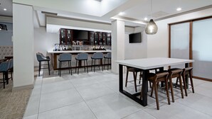 A modern kitchen with a bar area, a dining table with chairs, and a TV mounted on the wall. - Hilton Garden Inn Albuquerque Airport (Albuquerque)