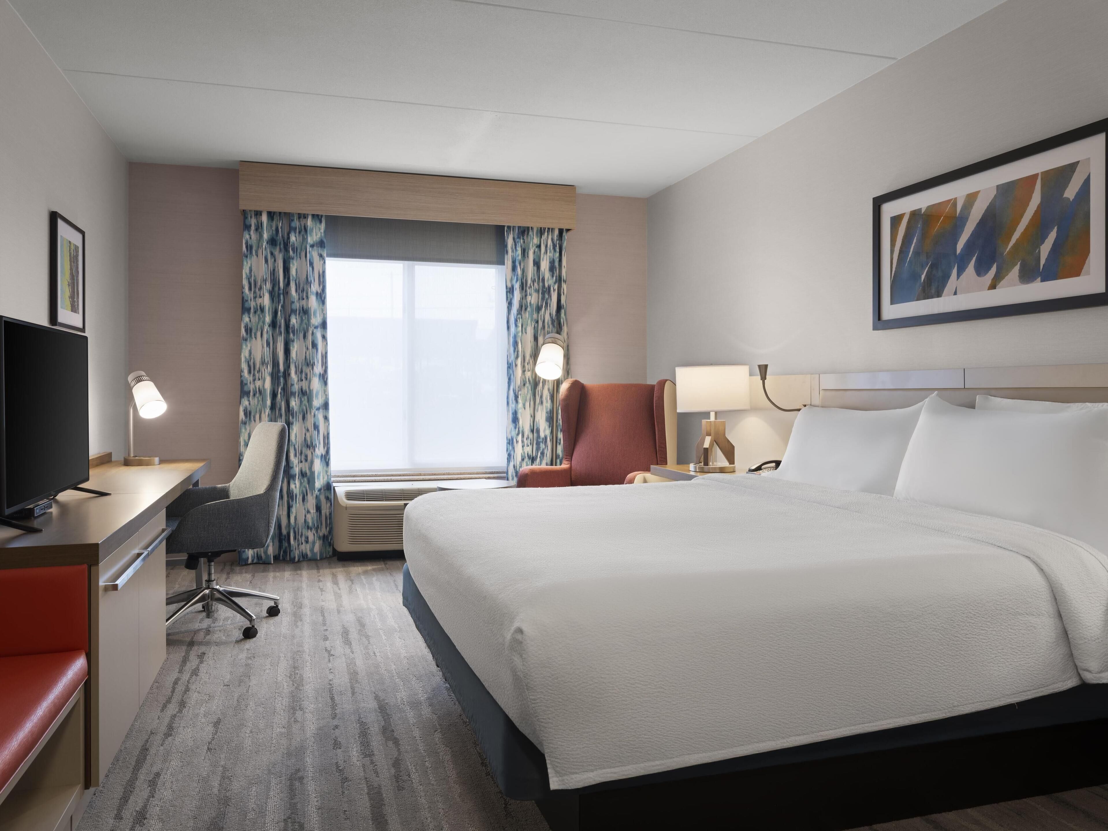 A hotel room with a bed, desk, chair, TV, and a window with curtains.
