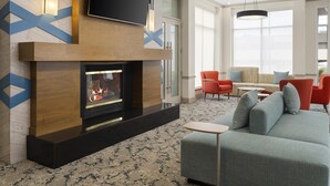 A modern living room with a fireplace, a flat-screen TV mounted above it, and a seating area with a sofa and chairs. - Hilton Garden Inn Albuquerque Airport (Albuquerque)