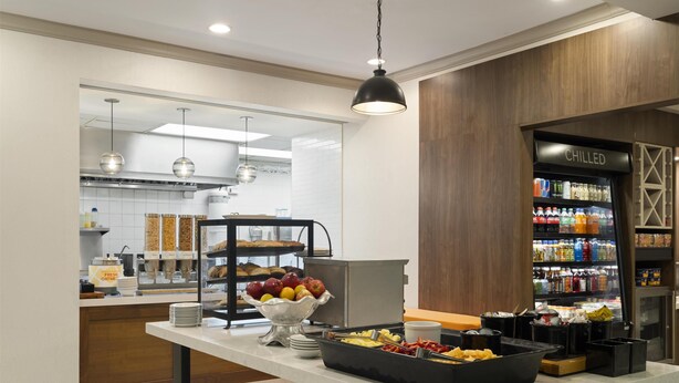A modern breakfast area with a buffet table, a fruit bowl, and a refrigerator labeled "CHILLED". - Hilton Garden Inn Albuquerque Airport (Albuquerque)