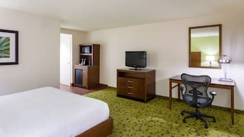 Una habitación de hotel con una cama, un escritorio con computadora y silla, un televisor y un espejo.