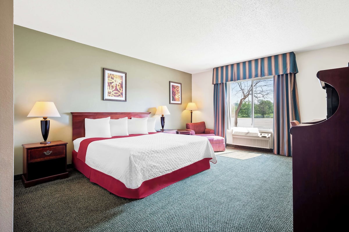 Habitación de hotel con una cama grande, dos mesitas de noche con lámparas, una ventana con cortinas y vistas al exterior.