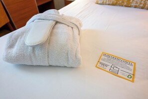 Una toalla blanca y una almohada sobre una cama, y un cartel con texto y logotipos.