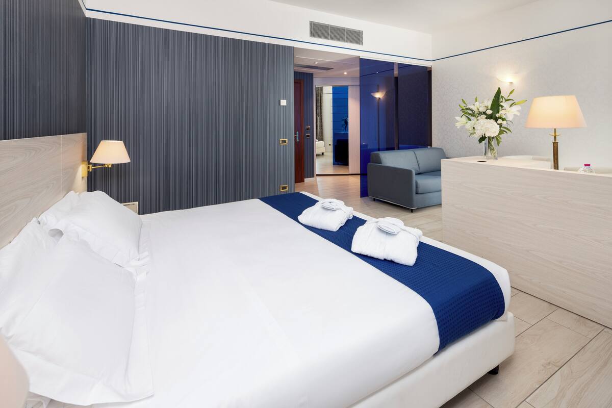 Une chambre d’hôtel avec un grand lit, un bureau, une chaise et une salle de bain visible à travers une porte ouverte.