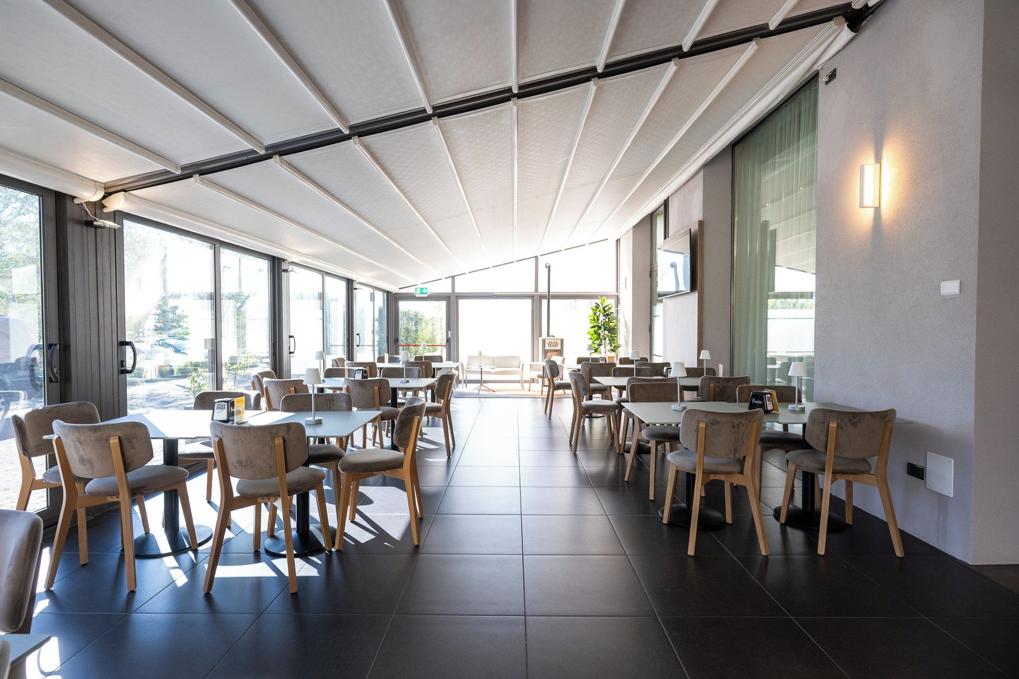 A modern dining area with tables and chairs, large windows, and a ceiling with a light fixture.