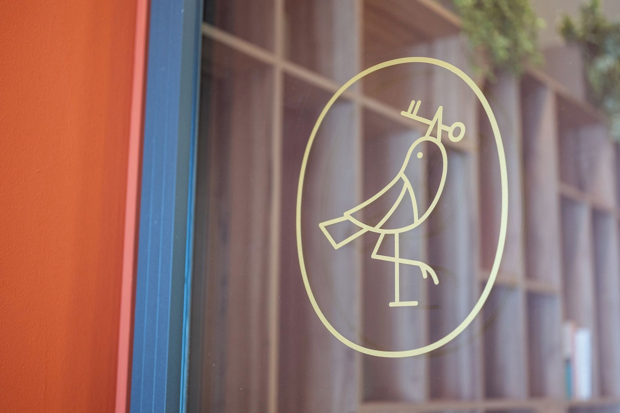 Ein Vogel-Symbol auf einer Glasscheibe, im Hintergrund unscharf das Innere eines Gebäudes zu sehen.
