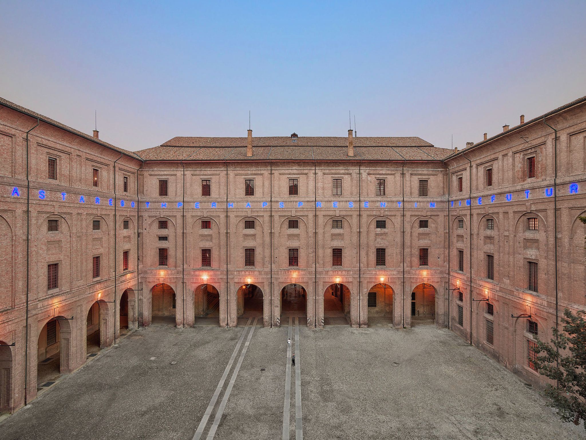 A large, historic building with a central courtyard, multiple arches, and a tiled roof.