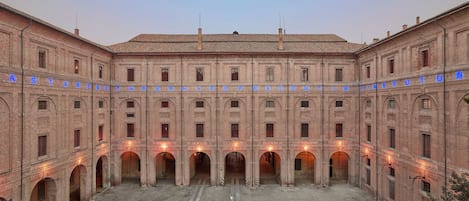 A large, historic building with a central courtyard, multiple arches, and a tiled roof.