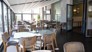 Un amplio comedor interior con varias mesas y sillas, ventanas grandes y un diseño moderno en el techo.