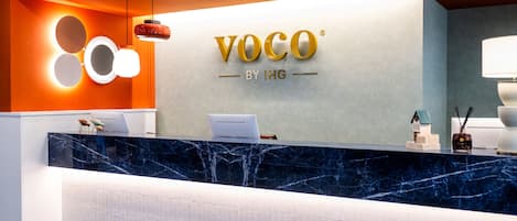 Uma mesa de recepção com tampo de mármore, um logotipo acima dela e uma luminária moderna no teto.