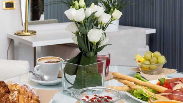 Una mesa de desayuno con croissants, café, fruta y un florero con flores.