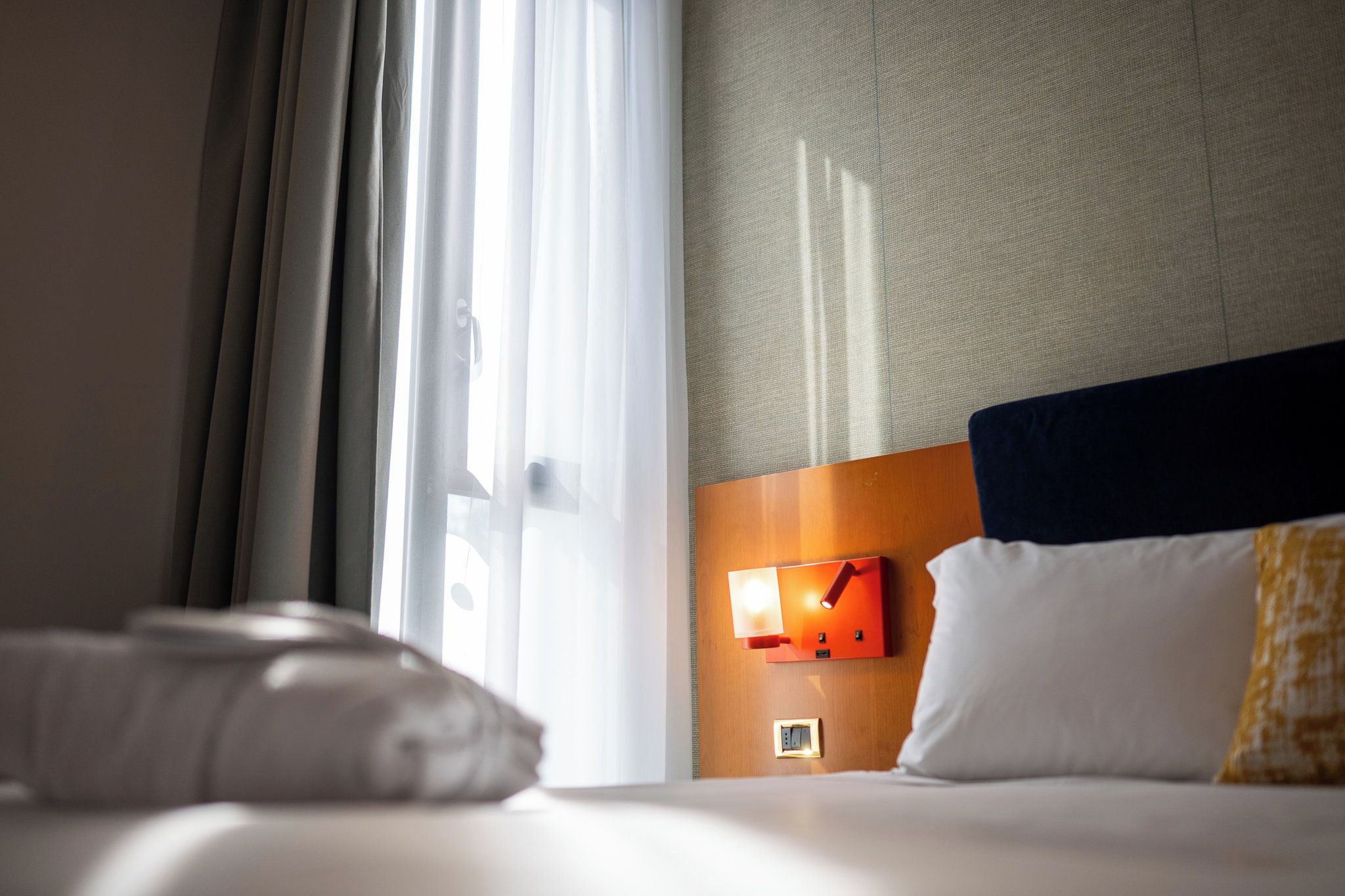 Una habitación de hotel con una cama, una mesita de noche con lámpara y una ventana con cortinas.