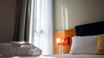 Ein Hotelzimmer mit einem Bett, einem Nachttisch mit Lampe und einem Fenster mit Vorhängen.