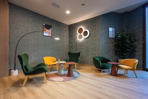 Un área de descanso moderna con sillones verde y amarillo, una mesa redonda y una planta grande en maceta.