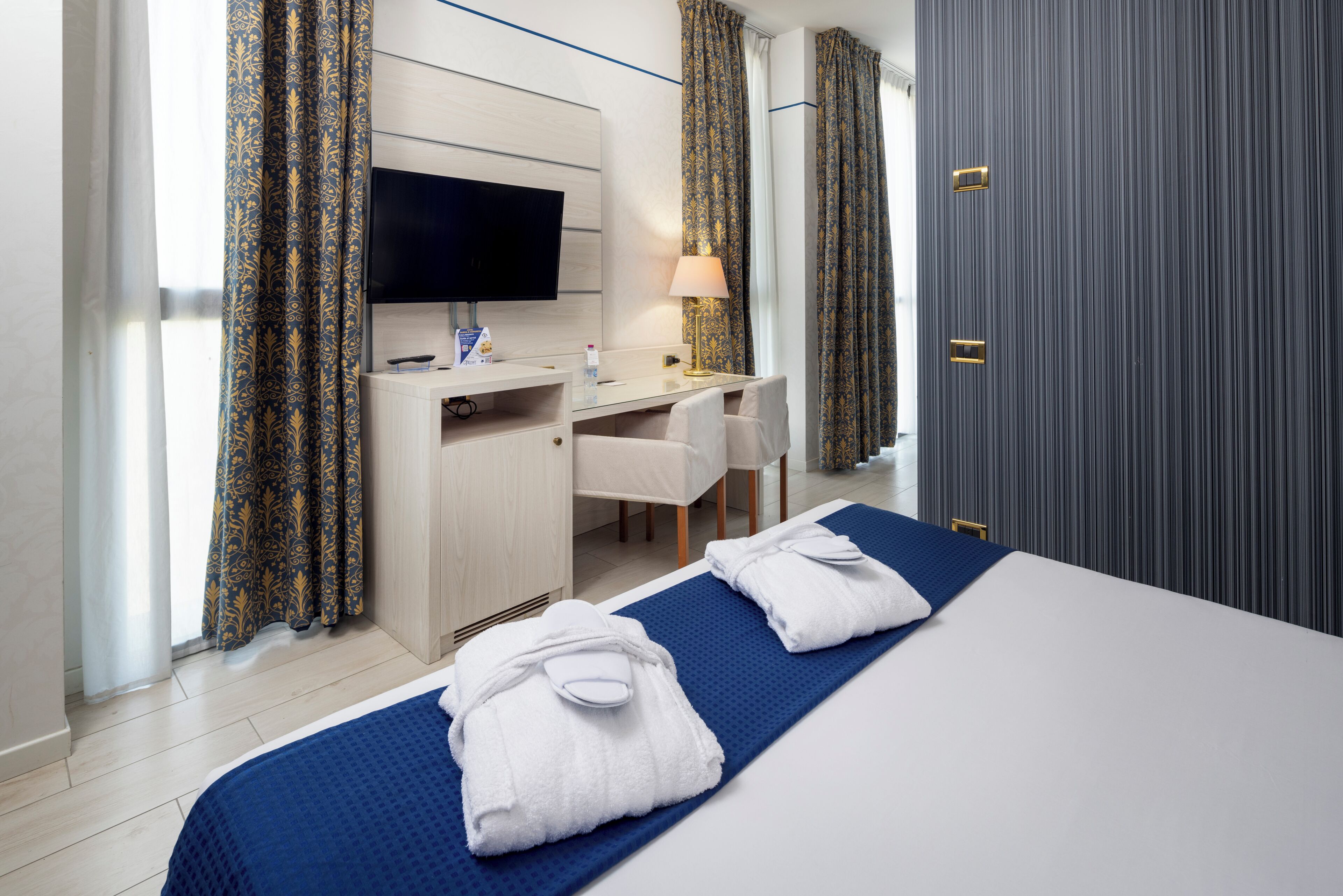 A hotel room with a bed, a desk, a television, and a wardrobe.
