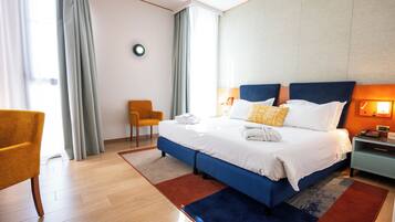 A hotel room with a bed, a chair, a bedside table, and a wall-mounted light.
