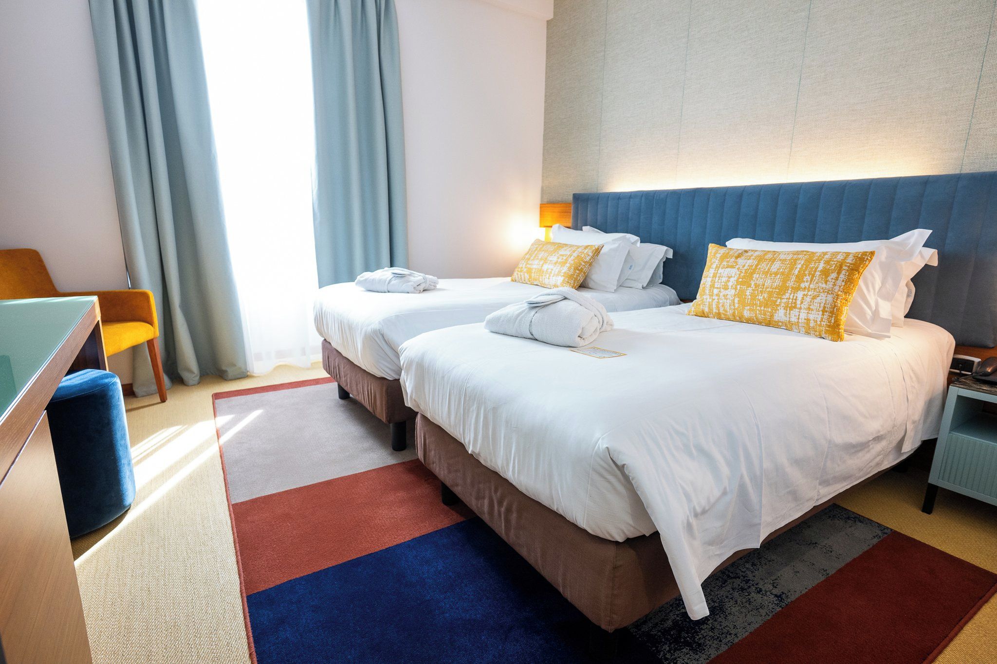 Una habitación de hotel con dos camas, un escritorio, una silla y una mesita de noche.
