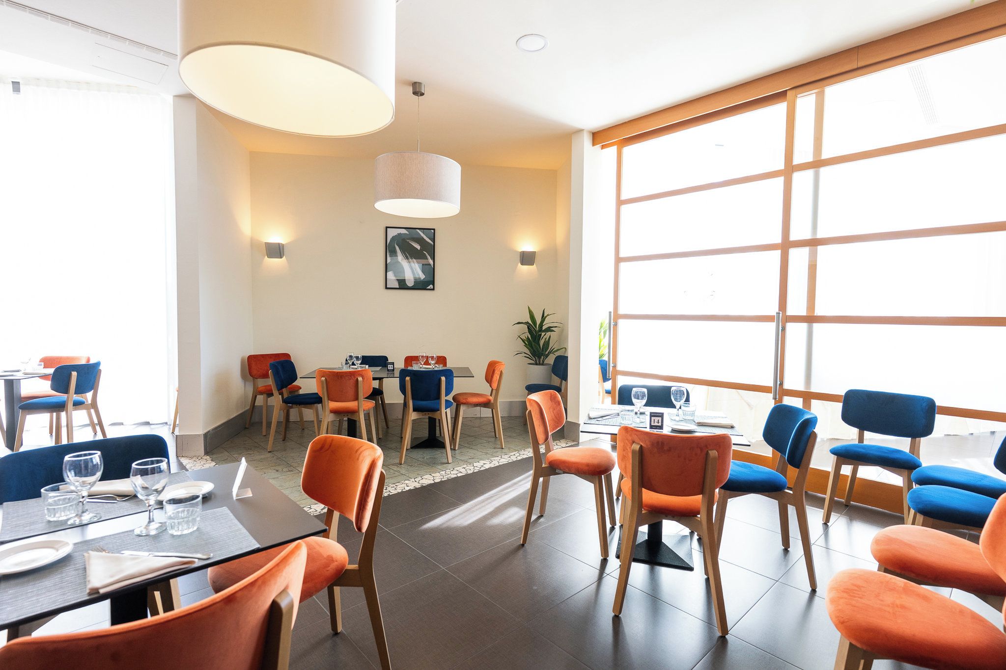 A modern dining area with tables and chairs, large windows, and a ceiling light fixture.