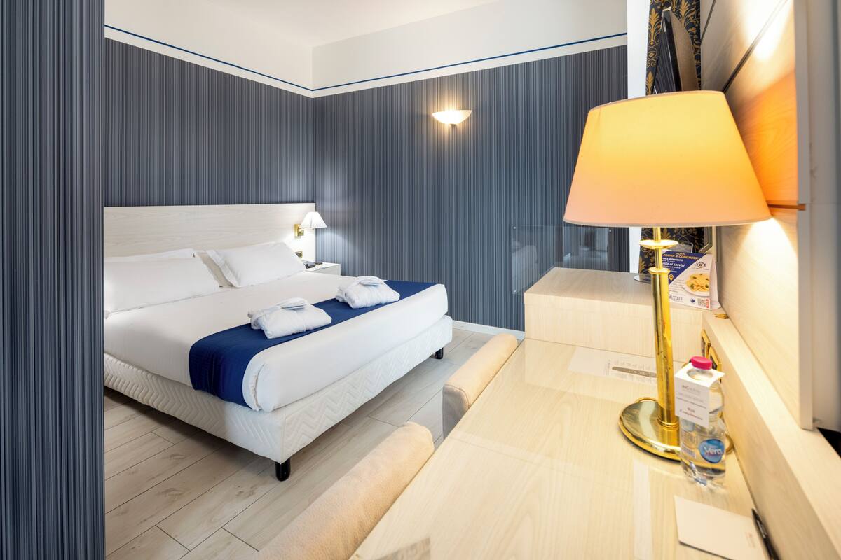 Une chambre d’hôtel comprenant un lit, une table de chevet, une lampe et un luminaire fixé au mur.