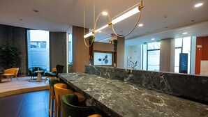 Una zona de recepción moderna con mostrador de mármol, varios taburetes y un amplio ventanal con vistas al exterior.