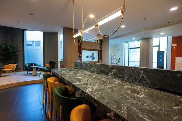 Un espace d’accueil moderne avec un comptoir en marbre, de nombreux tabourets de bar et une grande fenêtre offrant une vue sur l’extérieur.