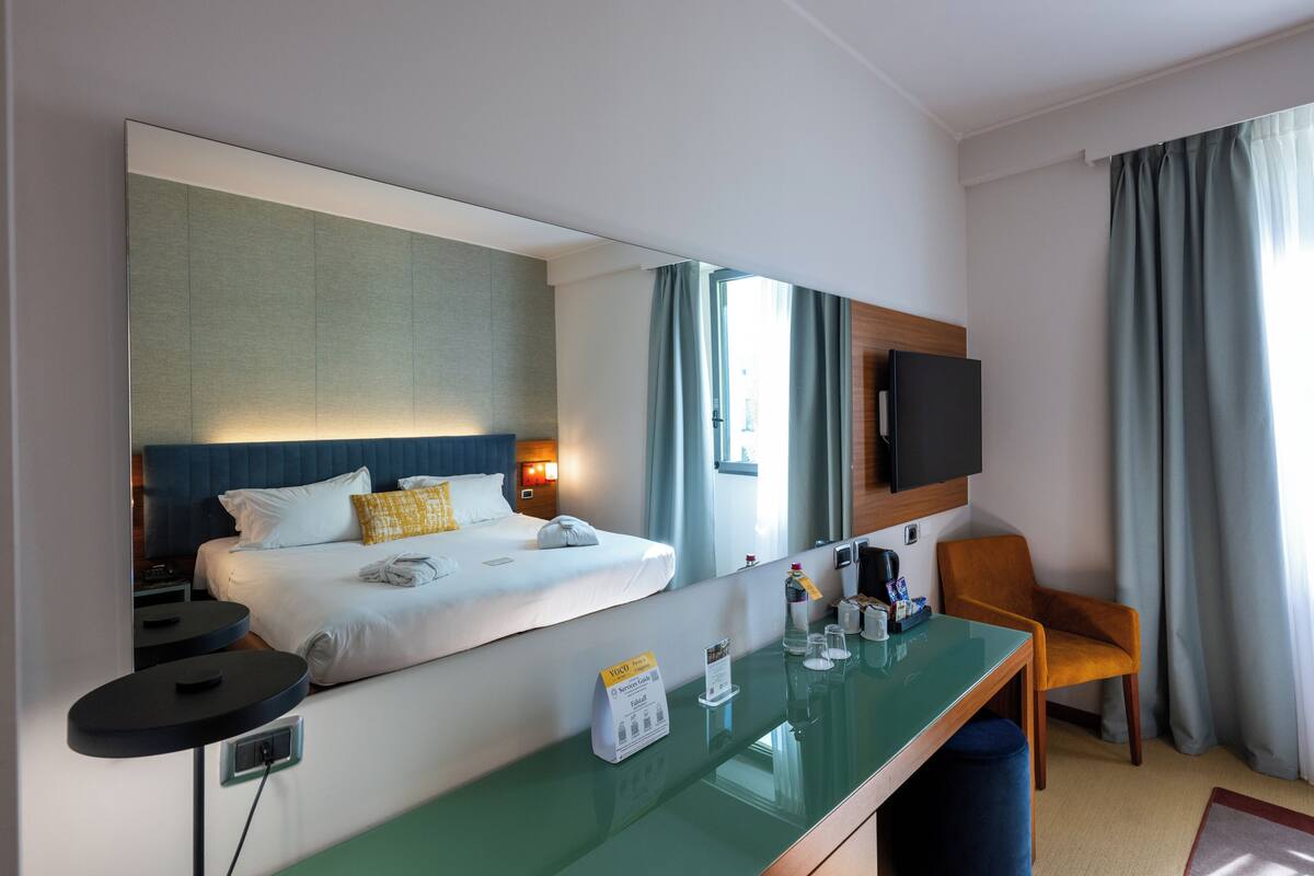 Une chambre d’hôtel comprenant un lit, un bureau avec une chaise, une télévision et un grand miroir.