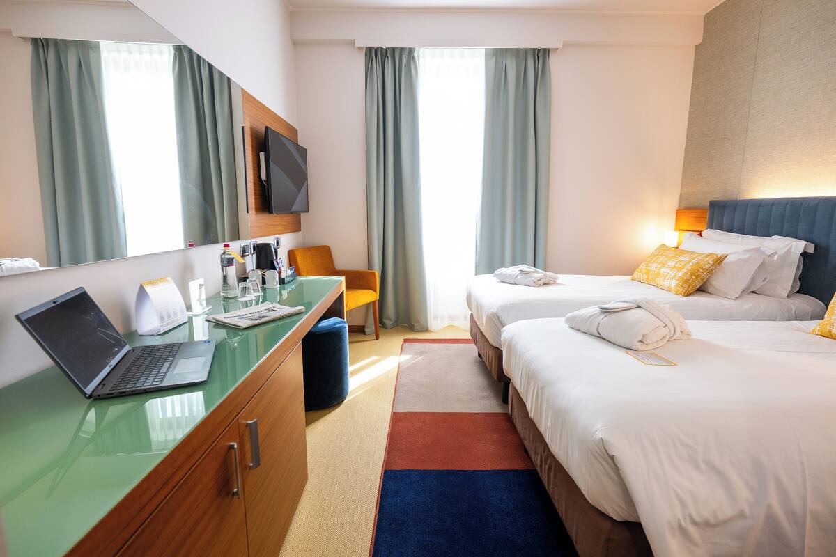 Une chambre d’hôtel équipée d’un bureau, de deux lits, d’une télévision et d’une fenêtre avec des rideaux.