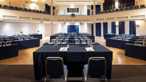 Un salón de conferencias con varias mesas, sillas y un balcón con cortinas azules.