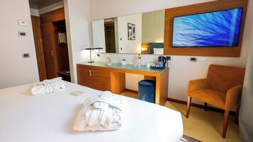 Quarto de hotel com cama, escrivaninha, cadeira, televisão e espelho.