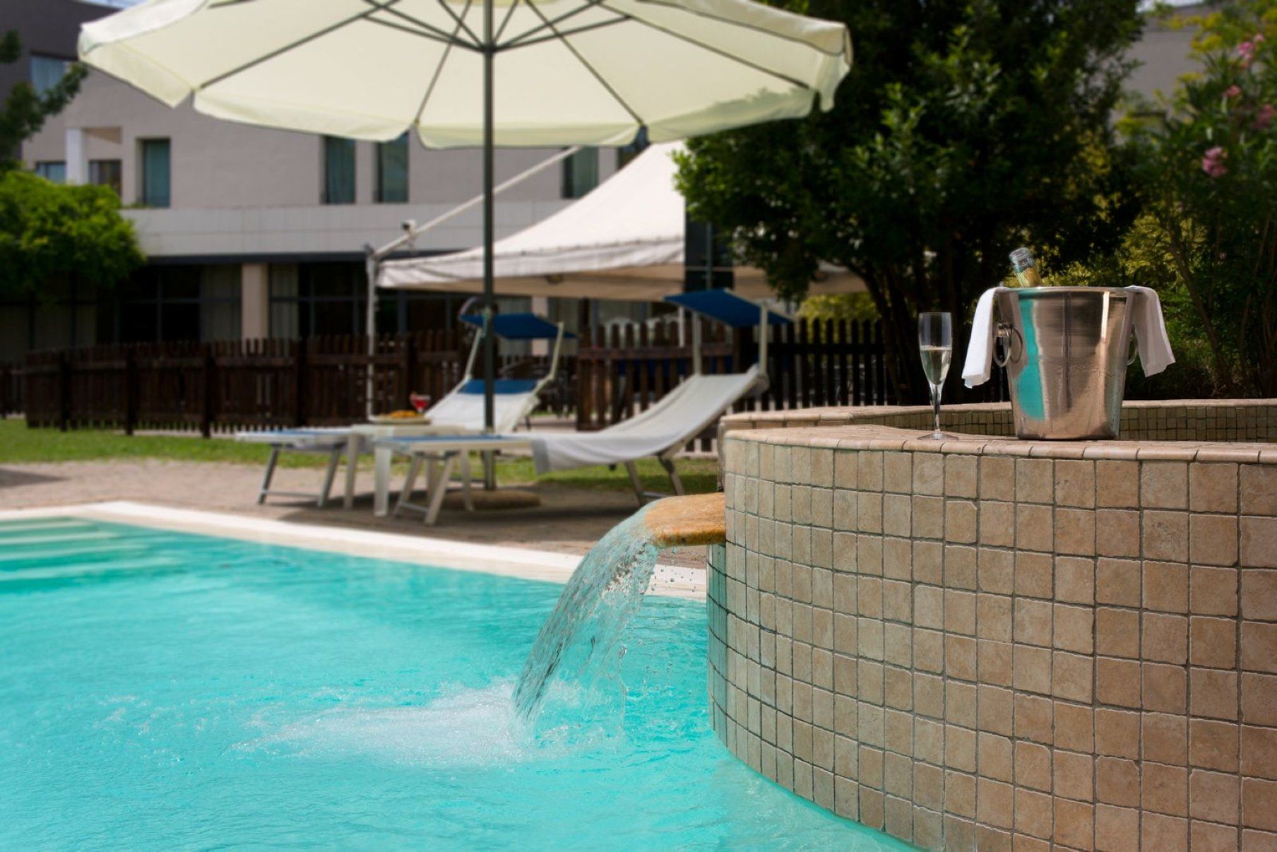A swimming pool with a tiled edge, lounge chairs, and a covered umbrella.