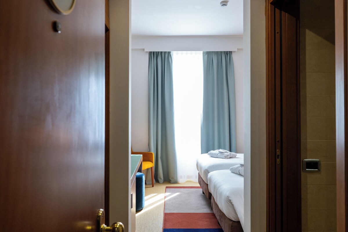 Une chambre d’hôtel avec un lit, un bureau et une fenêtre avec des rideaux.