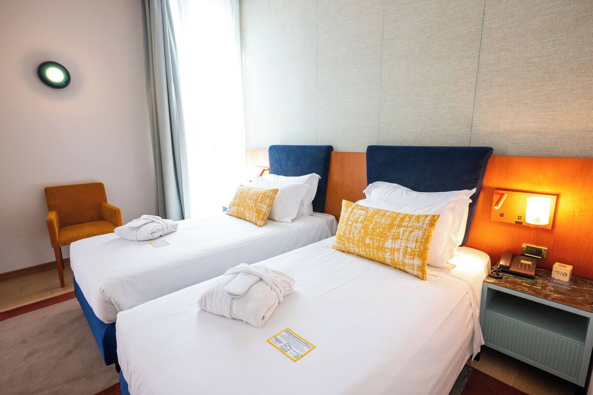 Une chambre d’hôtel avec deux lits, une chaise, une table de chevet et une lampe fixée au mur.