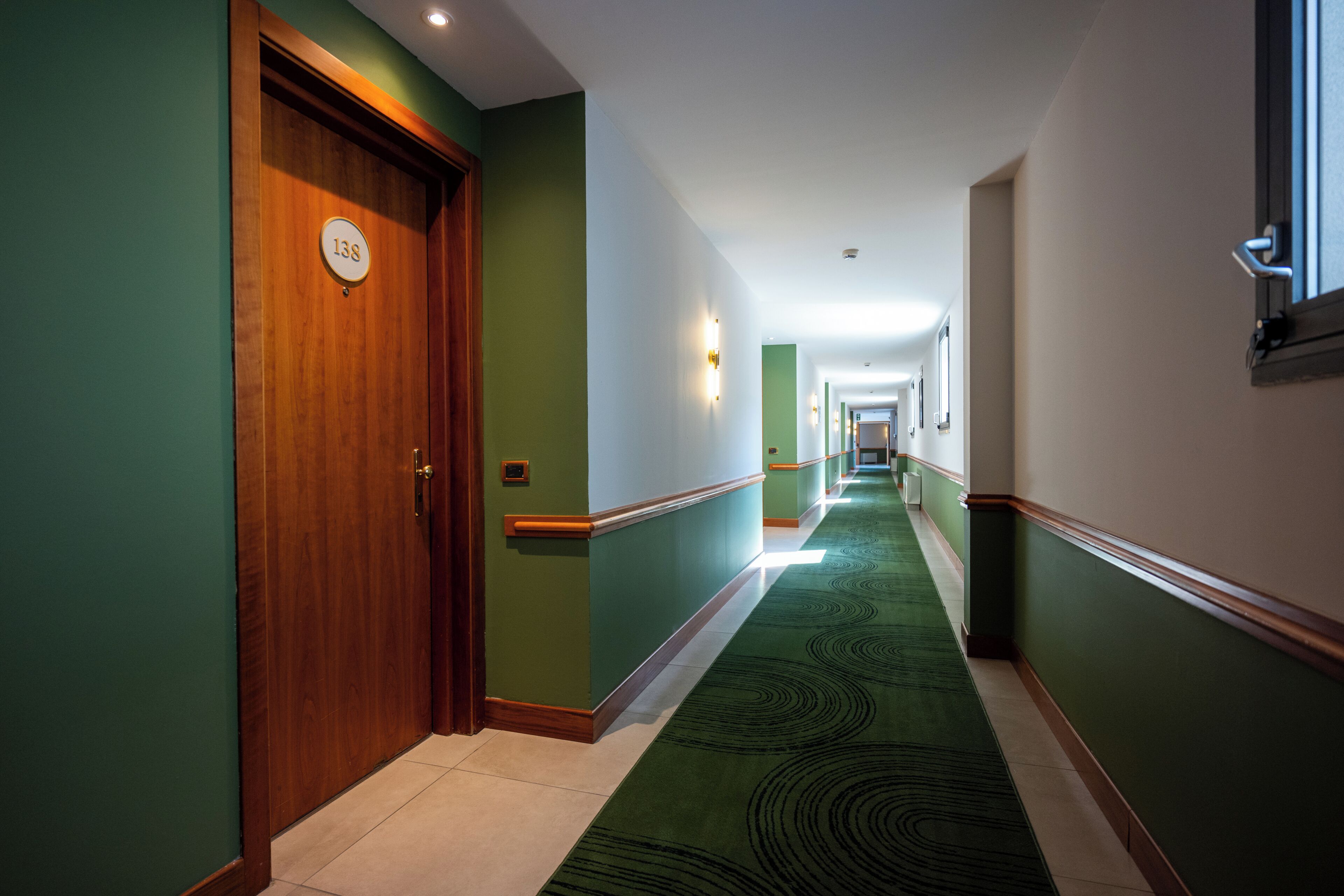 Un pasillo de hotel con alfombra verde, puertas de madera y un cartel que indica el número de habitación 138.