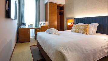 A hotel room with a bed, a desk, a wardrobe, and a TV.