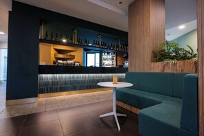 Zona de bar con barra, estantes llenos de botellas y un área de asientos con una mesa.