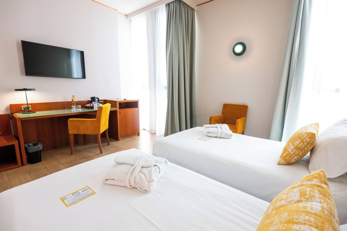 Une chambre d’hôtel avec deux lits, un bureau, une chaise, une télévision et une fenêtre avec des rideaux.