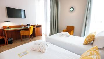 Habitación de hotel con dos camas, un escritorio, una silla, un televisor y un ventanal con cortinas.