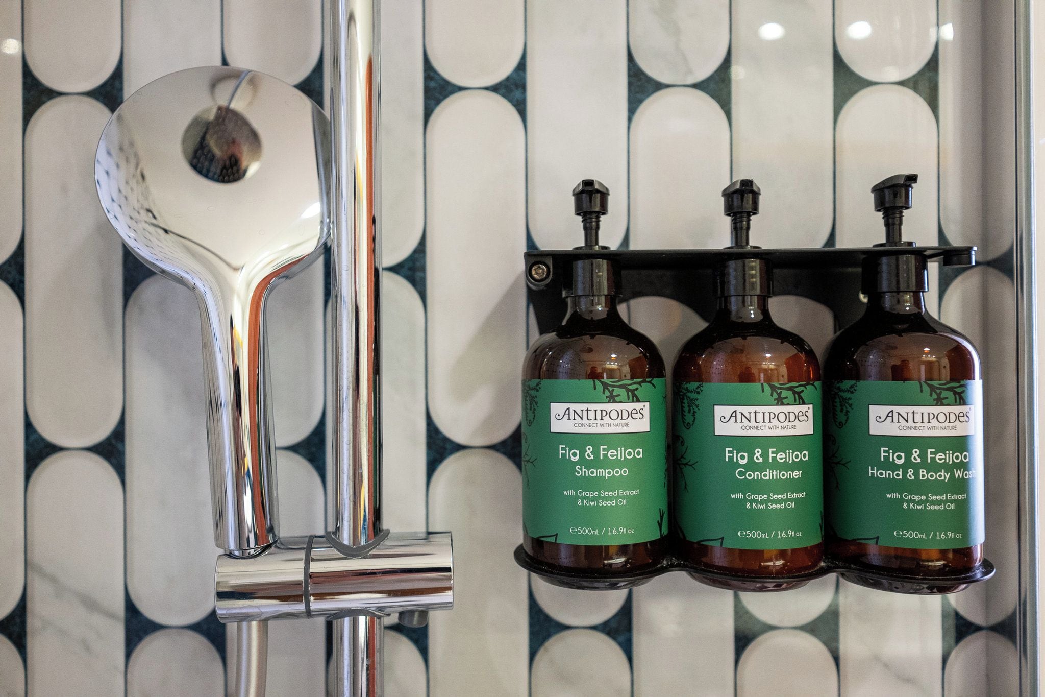 Un baño con un grifo cromado moderno y tres botellas de productos Antipodes en un dispensador de pared.