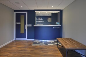 Un espace d’accueil avec un mur bleu, une horloge et un banc.