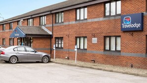 A Travelodge hotel with a brick facade, a car parked in front, and a clear sky. - Travelodge Sedgefield (Stockton-on-Tees)
