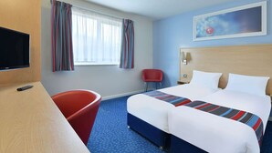 A hotel room with a bed, a desk with a TV, a red chair, and a window with curtains. - Travelodge Sedgefield (Stockton-on-Tees)
