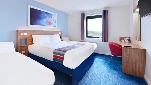 A hotel room with a bed, a desk, a chair, a TV, and a window with curtains. - Travelodge Sedgefield (Stockton-on-Tees)